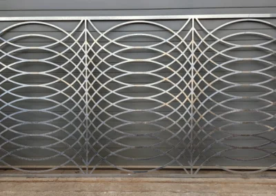 Large metal gate with intricate geometric patterns against a gray wall