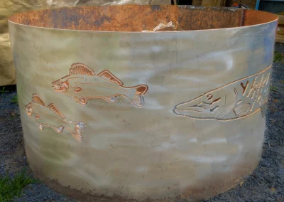 Rusty metal fire pit with cut-out fish designs against a blurred background